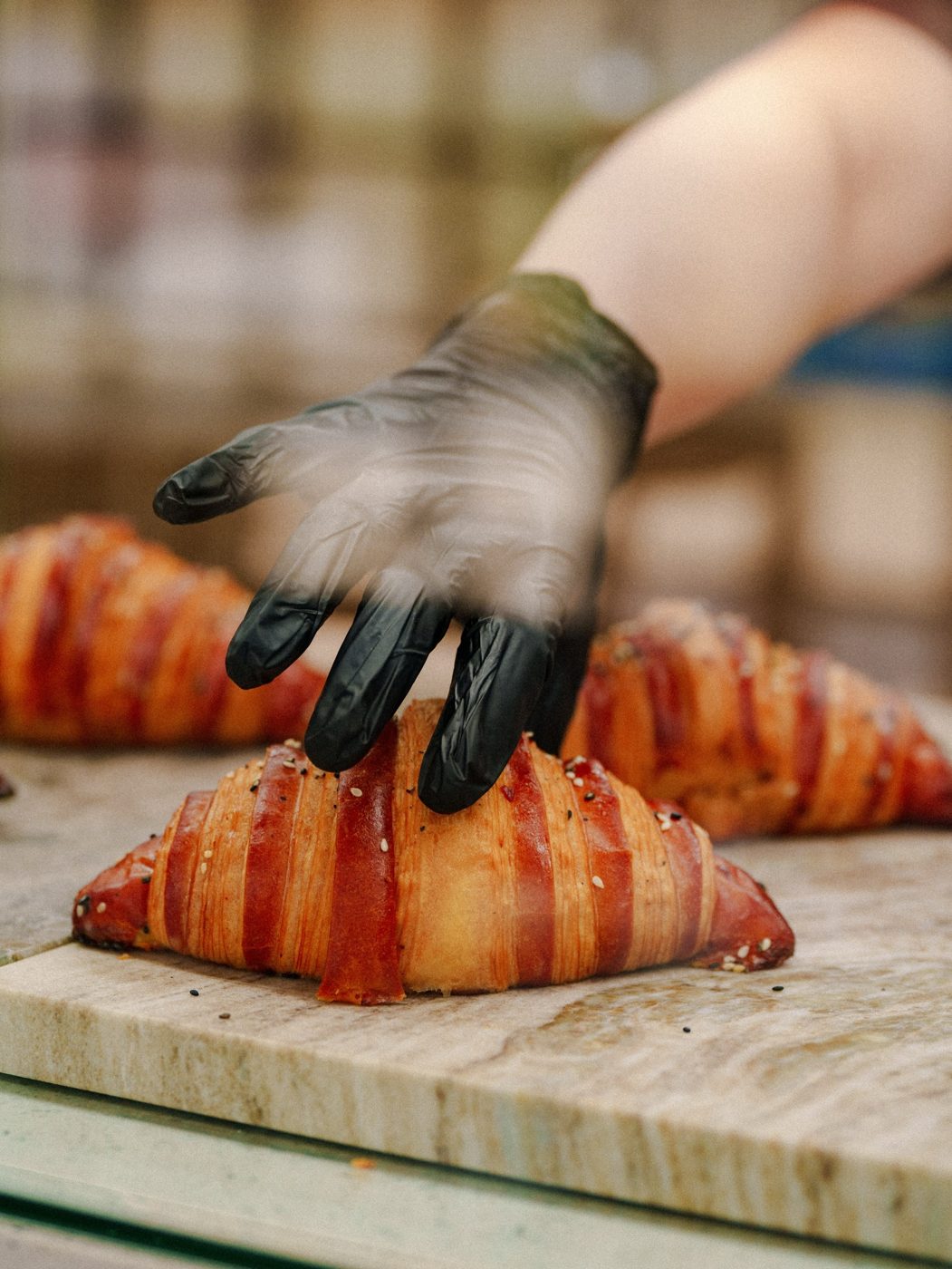 A gloved hand placing fresh croissants