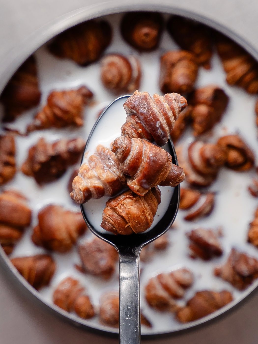 A spoon lifting mini croissants from a bowl of milk